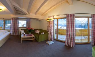 A modern room with two beds and a cozy seating area. Large windows offer a view of the mountains and allow plenty of daylight.