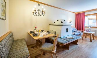 A cozy room with wooden furniture and a traditional stove. The table is lovingly set, and there are large windows with natural light.