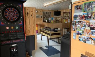 A cozy recreation room with a dartboard and a foosball table. Photos hang on the walls, and there are TVs and seating options.