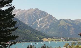A beautiful lake surrounded by green hills and mountains. Sailboats glide over the water.