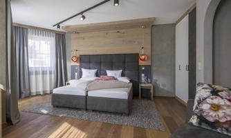 A modern bedroom with a large double bed and elegant wooden accents. Large windows provide plenty of daylight and a cozy atmosphere.