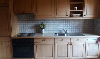 A cozy kitchen with wooden cabinets and a modern stove. The sink area is tidy and has a small floral decoration.