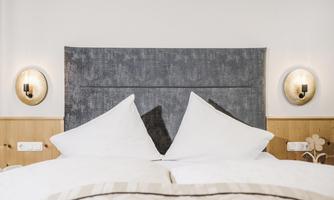 A cozy bedroom with a comfortable bed and bright cushions. The walls are in natural wood colors, and there are decorative wall lights.