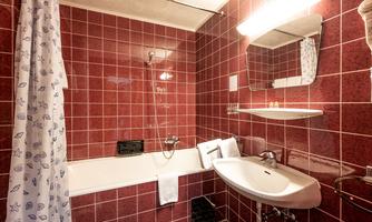 A bathroom with red tiles, a bathtub, and a sink. There is a shower curtain and a large mirror.
