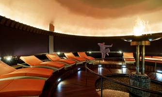 A relaxing quiet room with orange loungers and soft lighting. In the center, there is a fireplace that creates a cozy atmosphere.
