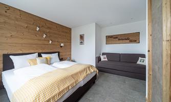 A modern bedroom with a large bed and a comfortable sofa. The walls are partially clad with wood, creating a cozy atmosphere.