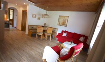 A cozy living area with red sofas and a dining area. The room has wooden ceilings and large windows that let in plenty of daylight.