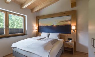 A cozy bedroom with a large bed and wooden ceiling. The window offers a view of nature and a stunning landscape painting hangs on the wall.