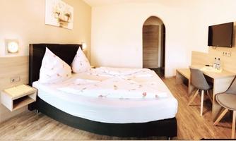 A modern room with a double bed and bright walls. There is a table, chairs, and a television, as well as a door that leads to another room.