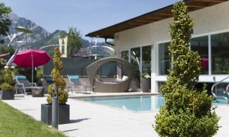 A beautiful outdoor area with a pool and modern loungers. Lush plants and a pavilion create a relaxed atmosphere.