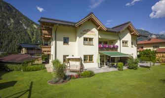 A charming house with a well-kept garden and a view of the mountains. It has an inviting outdoor area with a porch and flowers.