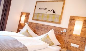 A cozy bedroom with two beds and rustic wood paneling. On the wall hangs a picture with the inscription "MOUNTAIN HAPPINESS" and a mountain symbol.