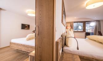 A modern bedroom with two separate wooden beds. The room features large windows and a friendly atmosphere.