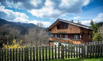 A traditional wooden house in a picturesque mountain landscape.  
In the foreground, there is a green garden with a wooden fence.