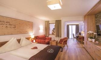 A cozy room with a large bed and a seating area. The warm wood tones and inviting decoration create a relaxed atmosphere.