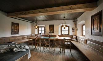 A traditional dining room with wooden décor and a long table. The brightness comes from the windows and the light fixtures.