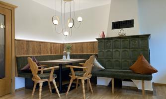 A cozy dining area with a green bench and a round table. A modern pendant light hangs on the wall.