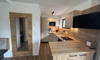 A modern kitchen with wooden surfaces and white cabinets. Plenty of daylight comes through the window onto the countertop.