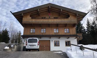 A traditional wooden house with a bright basement and a balcony. Surrounded by snow and trees, it conveys a cozy atmosphere in nature.