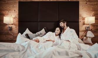 A couple relaxes in a cozy bed in bathrobes. The atmosphere is warm and inviting, with soft lighting and wooden decor.