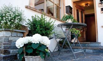 An inviting entrance area with a stone staircase and a table with two chairs. White hydrangeas and green plants in baskets are blooming in front of the door.