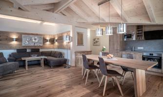 A modern living room with a wooden ceiling and a cozy seating area. The dining area is bright and inviting, with a large table and stylish chairs.