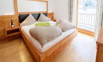A cozy bedroom with a large bed and wood paneling. Large windows provide plenty of daylight and a view outside.