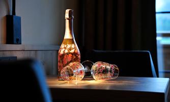 A bottle of rosé wine is on a table, next to it are two glasses. The light highlights the colors of the bottle and glasses, creating a cozy atmosphere.