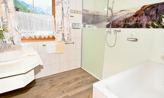 A modern bathroom with a shower cabin and a bathtub. Large windows provide a beautiful view of the surrounding nature.