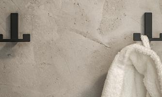 A modern wall with two black hooks. A white bathrobe hangs from one hook.