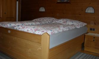 A cozy bedroom with a wooden bed and colorful bedding. The walls are made of wood and there is a bedside lamp.