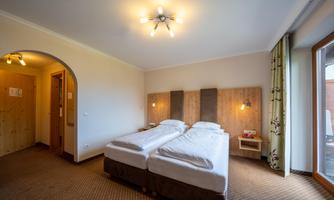 A bright bedroom with two single beds and cozy furnishings. Large windows provide plenty of light and a view outside.