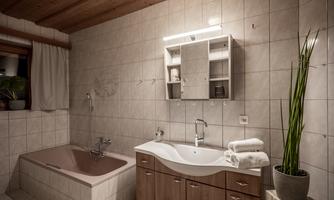 A modern bathroom with a bathtub and an elegant sink. The walls are light-tiled, and a plant provides a fresh accent.
