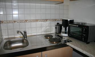 A modern kitchen with a sink, stovetops, and various kitchen appliances. Next to the sink, there is a microwave and a coffee machine on the countertop.