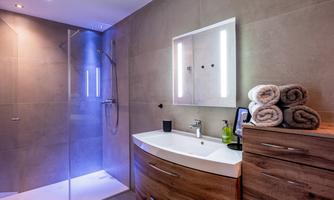A modern bathroom with a glass shower and soft lighting. Freshly folded towels are ready at the sink.