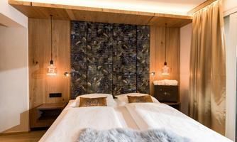 A modern bedroom with a double bed and wooden paneling. The walls are stylishly decorated and there is gentle lighting.