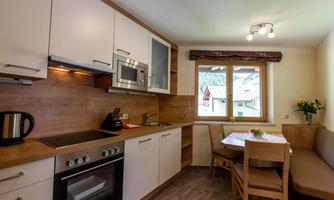 A modern kitchen with wooden details and white cabinets. There is a dining area with a table and chairs, as well as a window looking outside.