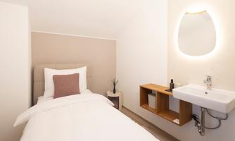A cozy single room with a bed and soft colors. There is a modern sink and stylish lighting.