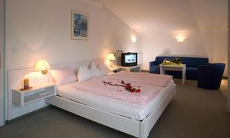 A romantic bedroom with a large bed, decorated with flower petals. The cozy furnishings include a television and a seating area.