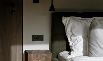 A modern bedroom with a comfortable bed and a wooden nightstand. The light gently falls on the bedding and the floor.