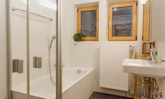 A modern bathroom with a shower and bathtub. The room has light walls and windows with wooden frames.