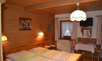 A cozy bedroom with wooden paneling and two beds. The room is furnished with a table, chairs, and a television.