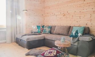 A cozy living room with a large gray couch and colorful cushions. The wooden wall and the wooden table create a warm atmosphere.