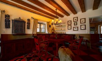 A cozy dining area with wooden beam ceiling and red painted chairs. Pictures hang on the walls and there is a rustic sideboard.