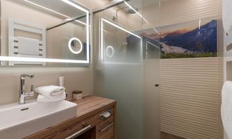 A modern bathroom with a glass shower and a wooden sink. The walls are bright, and the lighting creates a pleasant atmosphere.
