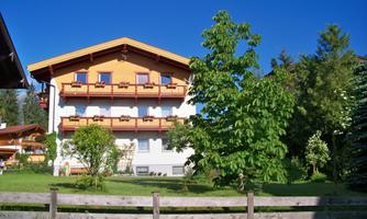An attractive house with wooden embellishments and balconies. The surroundings are green and inviting, ideal for a vacation in the mountains.
