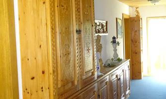 A narrow hallway with a tall, rustic wooden cabinet and a long sideboard. The walls are bright, and the floor is covered with blue carpet.