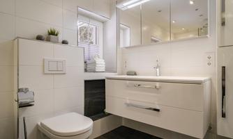 A modern bathroom with a white sink and a mirror. The walls are brightly tiled, and there is a large window opening.