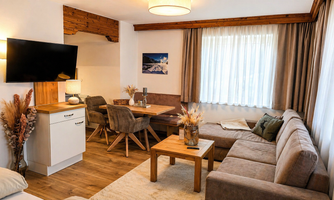A modernly furnished living room with a cozy couch and a wooden table. Large windows provide plenty of daylight and an inviting atmosphere.
