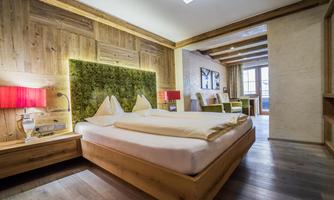 A modern bedroom with wood decor and a cozy double bed. The green wall decoration and the red lamps give the room an inviting atmosphere.